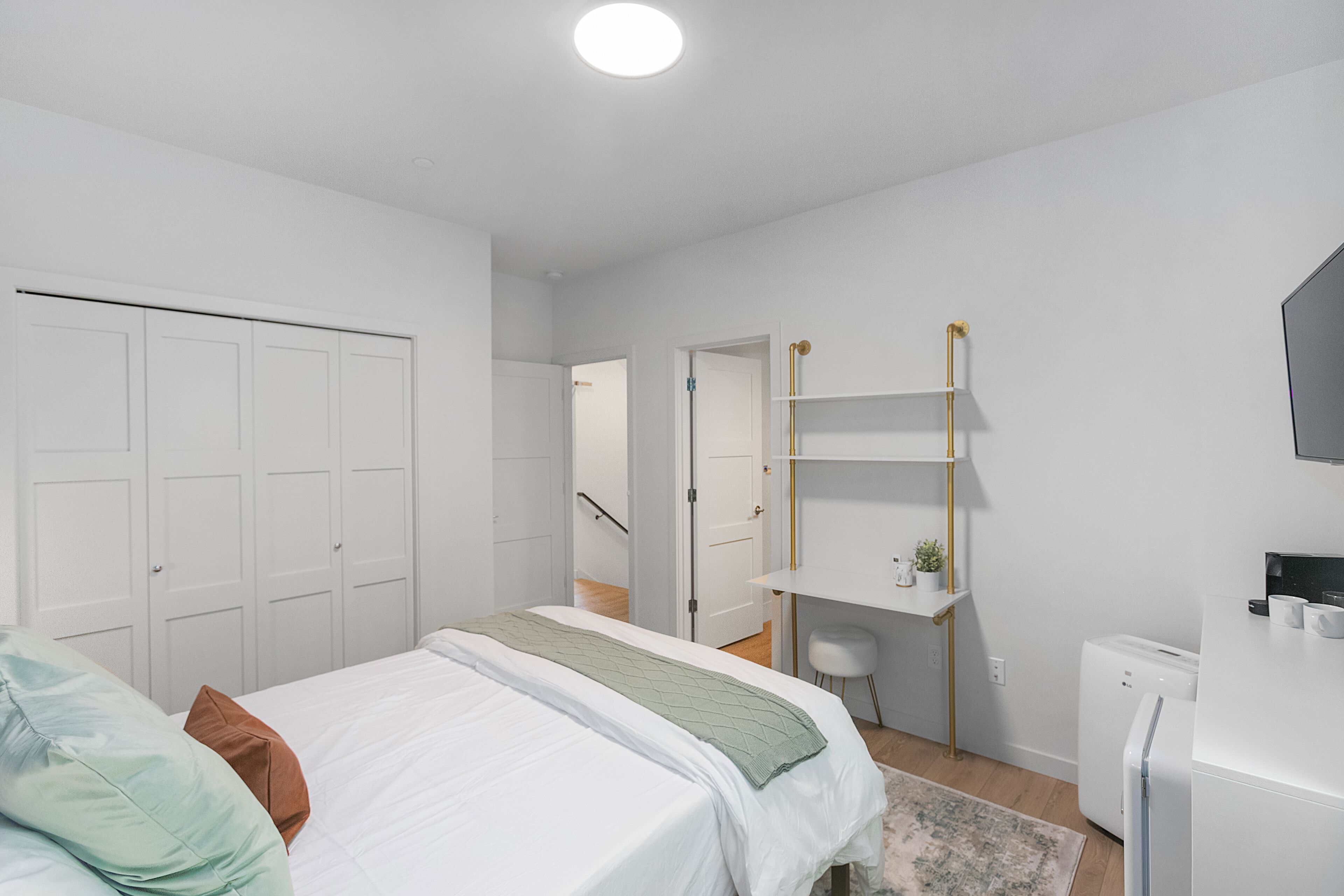 A modern bedroom with a bed, white wardrobe, and a small desk area with a chair.