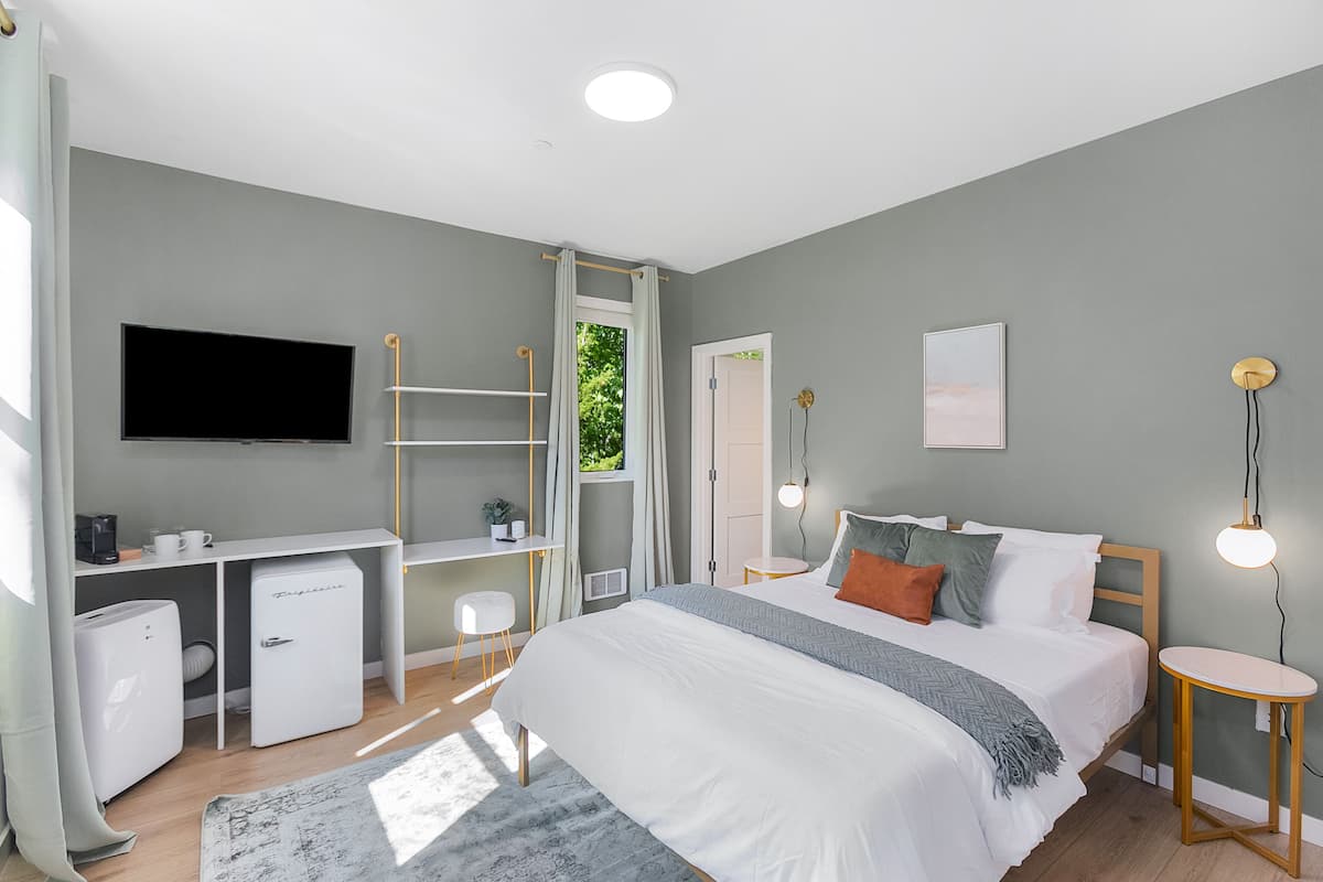 A bedroom with a bed, a desk, a TV, and a small table.