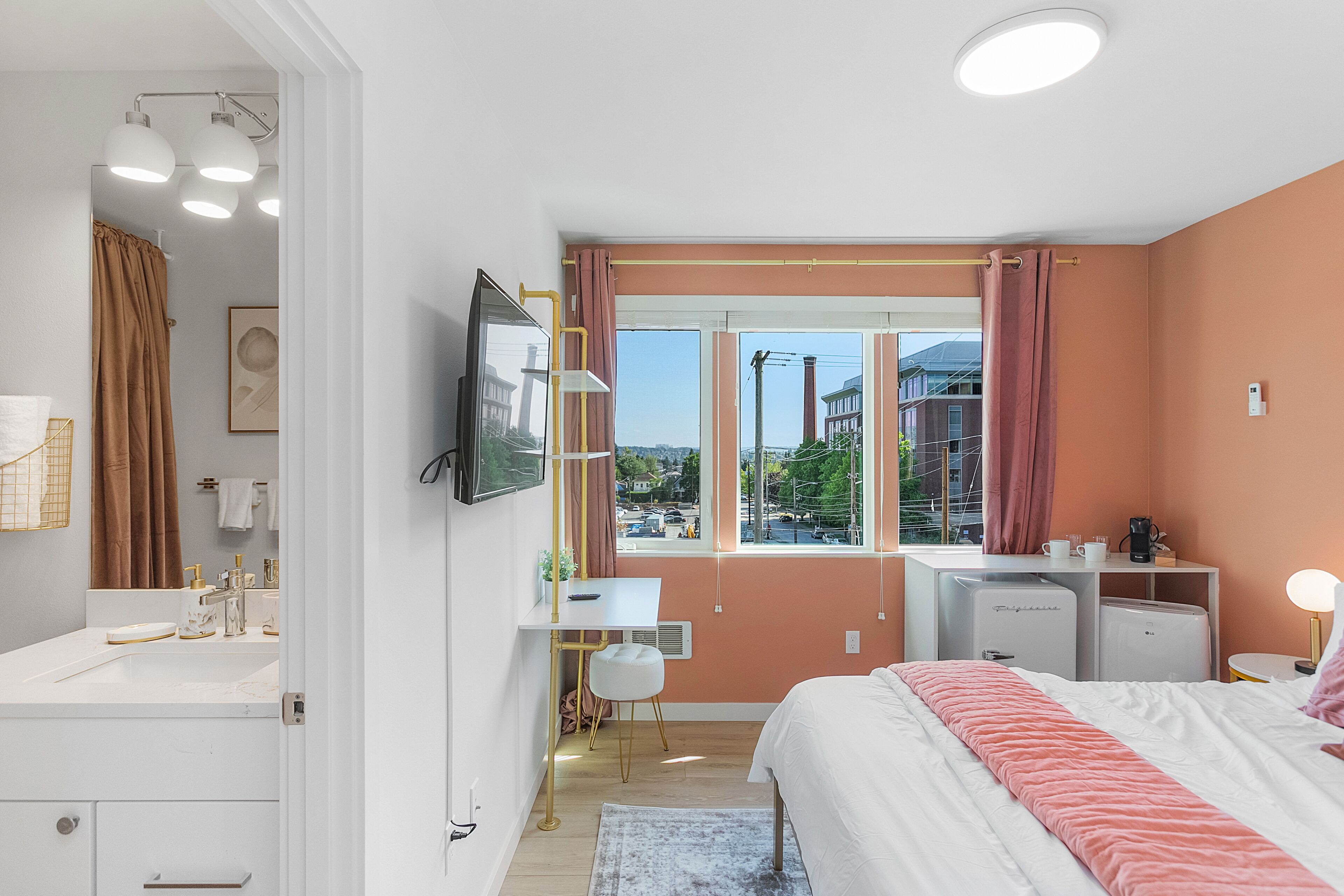 A modern bedroom with a bed, bedside table, desk, and a window with curtains.