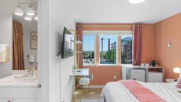 A modern bedroom with a bed, bedside table, desk, and a window with curtains.