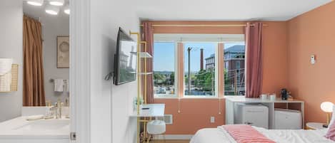 A modern bedroom with a bed, bedside table, desk, and a window with curtains.