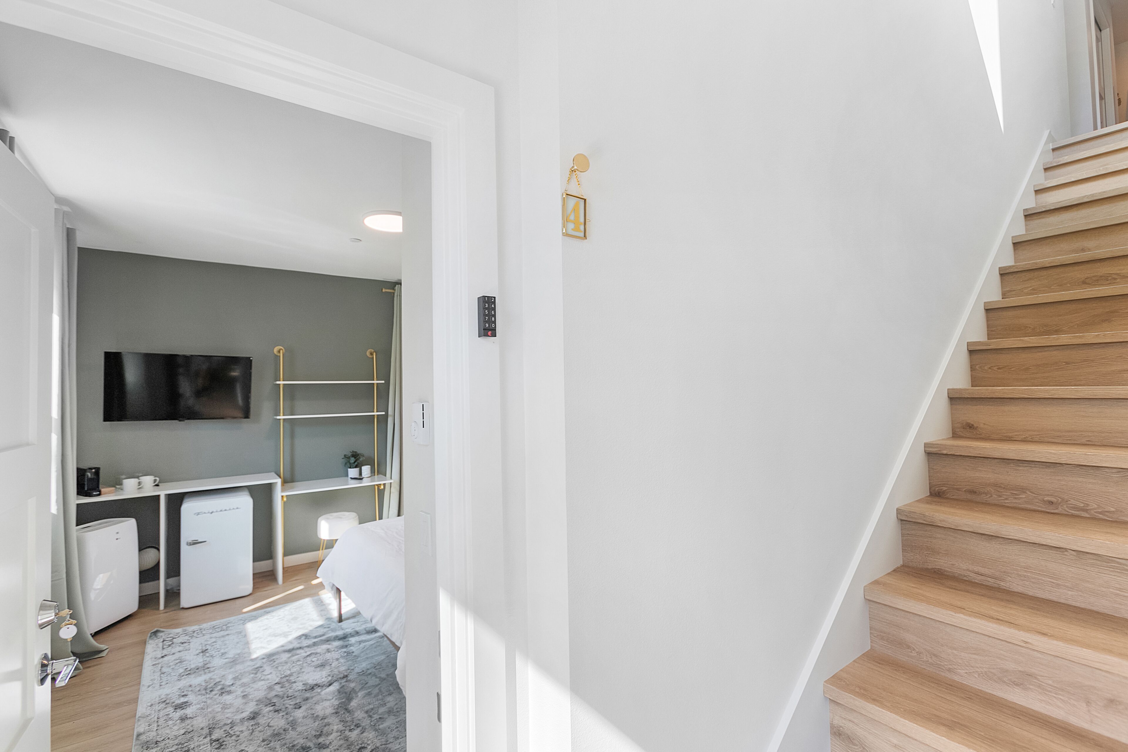 Un interior moderno con una escalera, un área de escritorio con televisor y un refrigerador pequeño.