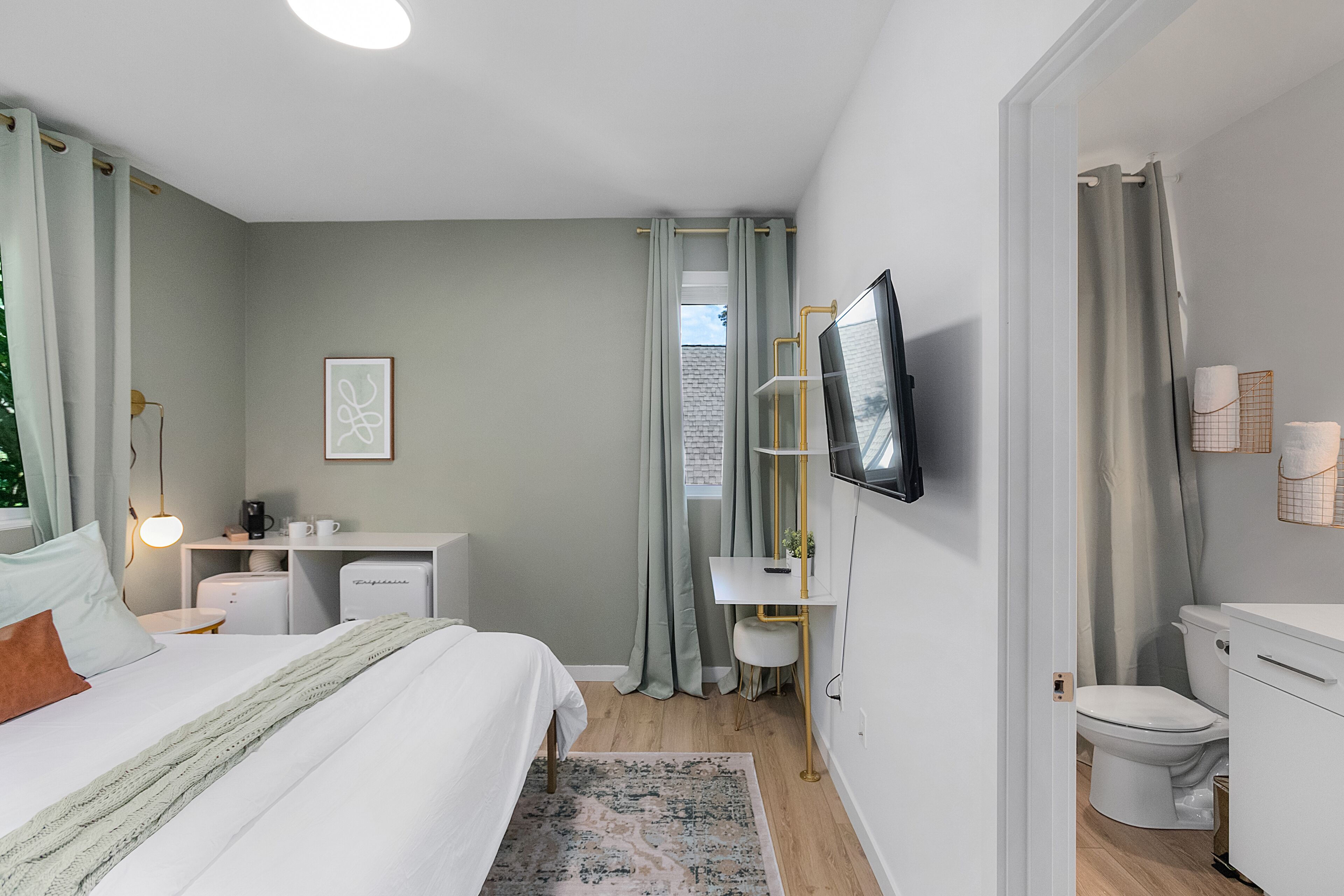 A modern bedroom with a bed, bedside table, desk, and a television.