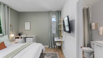 A modern bedroom with a bed, bedside table, desk, and a television.