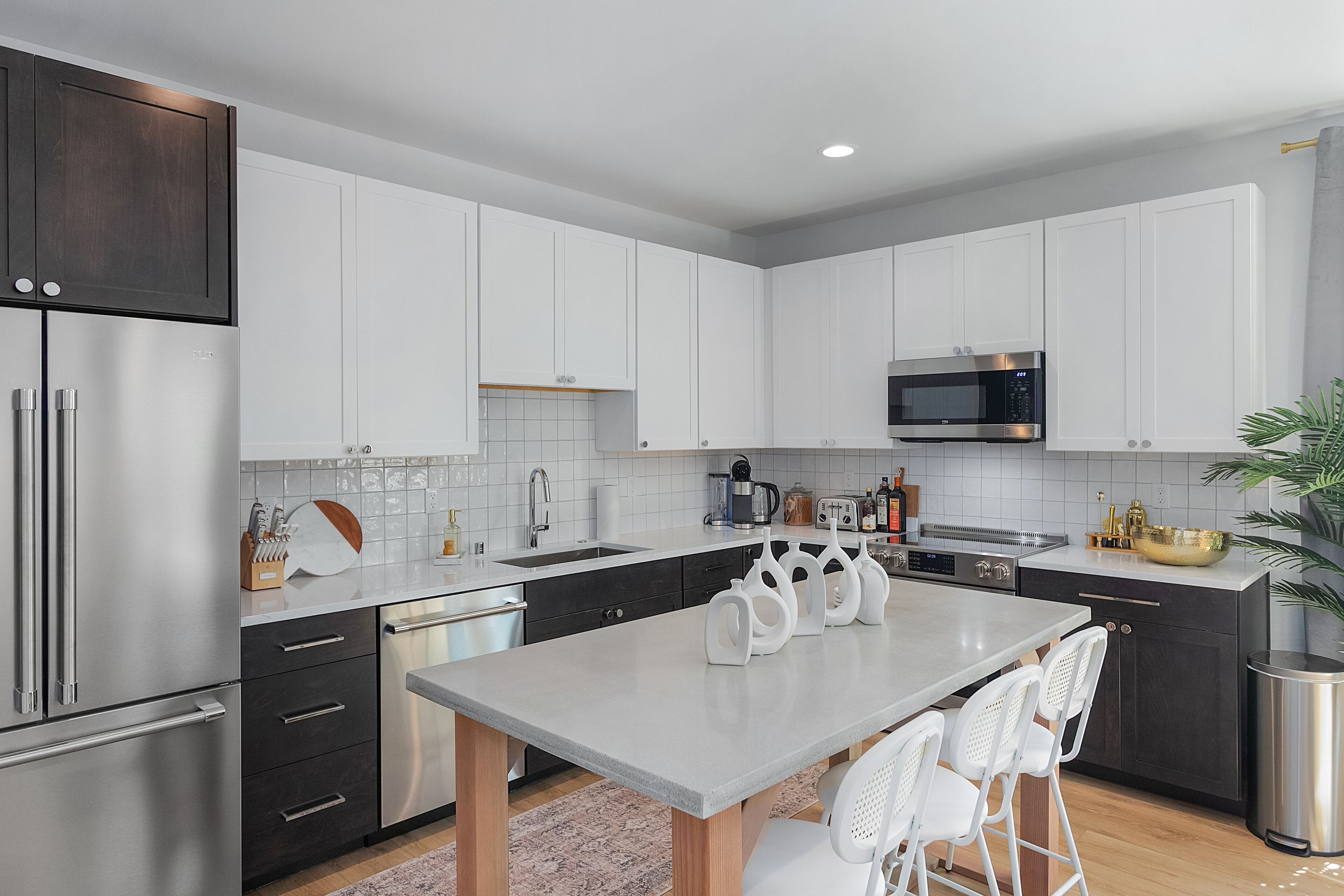 Una cocina moderna con armarios blancos, electrodomésticos de acero inoxidable y una isla central con sillas.