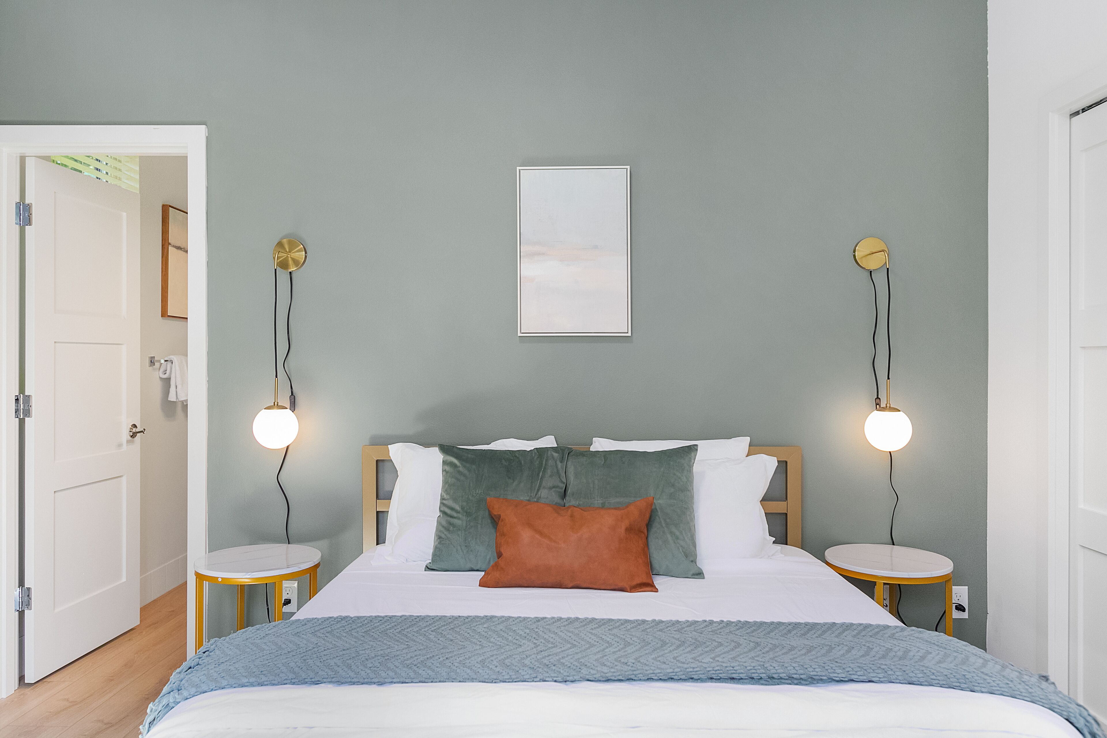 A bedroom with a bed, two bedside tables, a wall-mounted light, and a door.