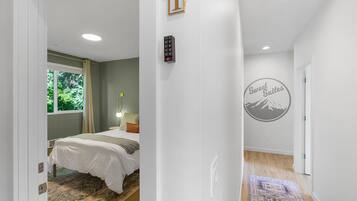 A hotel room with a bed, a bedside table with a lamp, a window with curtains, a wall-mounted phone, and a door with a sign.