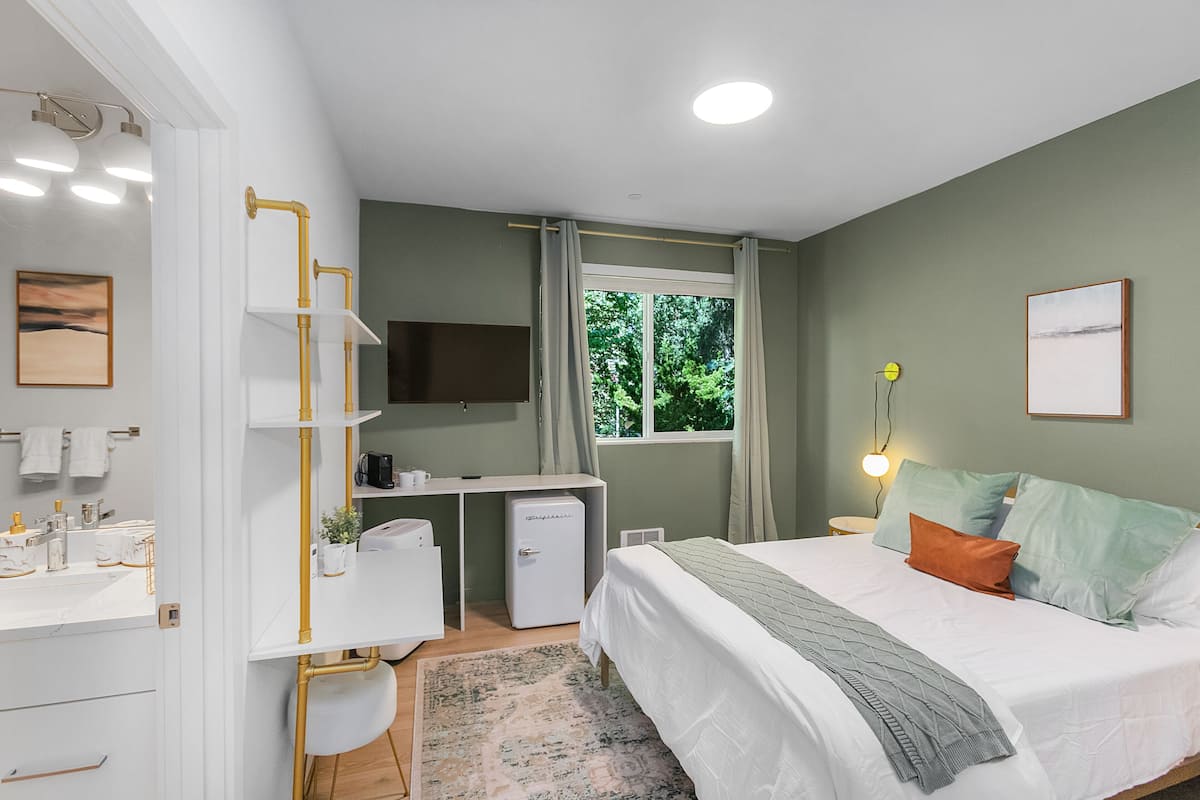 A bedroom with a bed, bedside table, desk, chair, and a window with curtains.