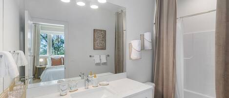 A modern bathroom with a large mirror, white vanity, and a shower area.