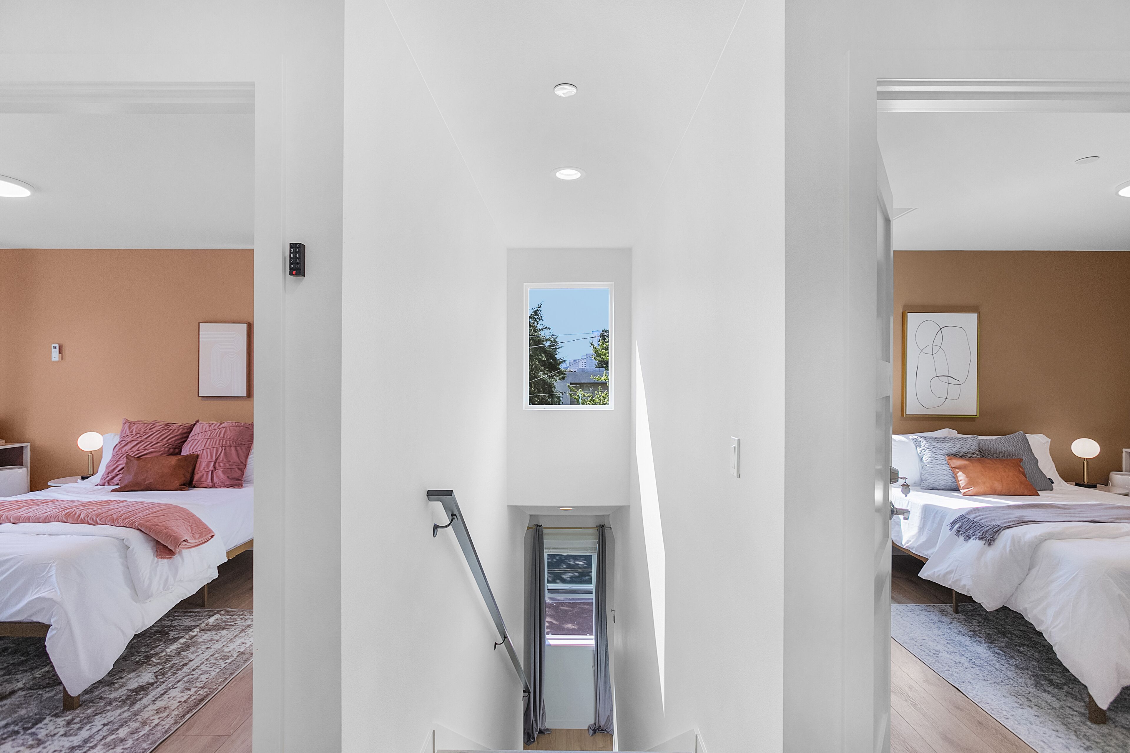 A modern bedroom with a large bed, a small window, and a staircase leading to another room.