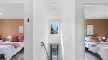 Une chambre moderne avec un grand lit, une petite fenêtre et un escalier menant à une autre pièce.