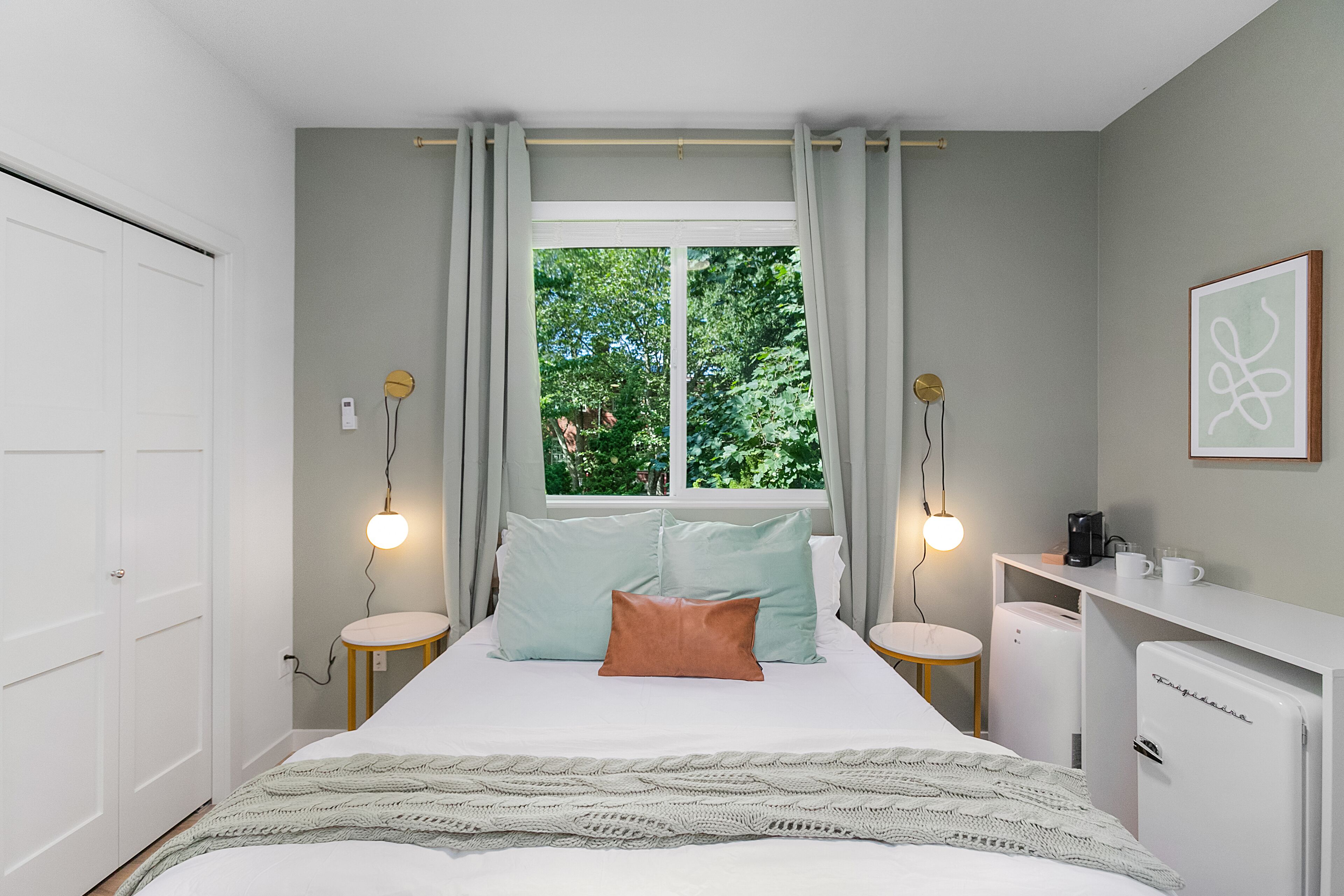 Ein Schlafzimmer mit Bett, Nachttischen, einem Schreibtisch, einem Kühlschrank und einem fenster mit Vorhängen.