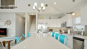 A modern kitchen with white cabinets, a large island, and blue chairs. - Summer Special! Views! Beachside, HotTub, Arcade, FirePit, Pets, Family Retreat (Galveston)