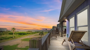 A wooden deck with chairs and a staircase leading to a balcony overlooking a beach at sunset. - Summer Special! Views! Beachside, HotTub, Arcade, FirePit, Pets, Family Retreat (Galveston)