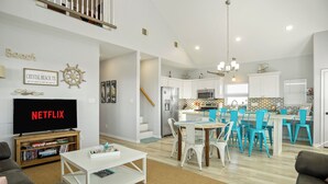 A modern living room with a flat-screen TV, a coffee table, and a bookshelf. - Summer Special! Views! Beachside, HotTub, Arcade, FirePit, Pets, Family Retreat (Galveston)