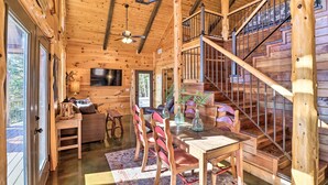 A wooden cabin interior with a dining area, a staircase, and a television. - Mountain View Hideaway w/ Outdoor Fireplace! (Mountain View)