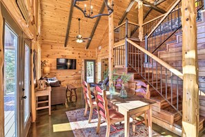 Ein Holzblockhaus-Innenraum mit Essbereich, einer Treppe und einem Fernseher.