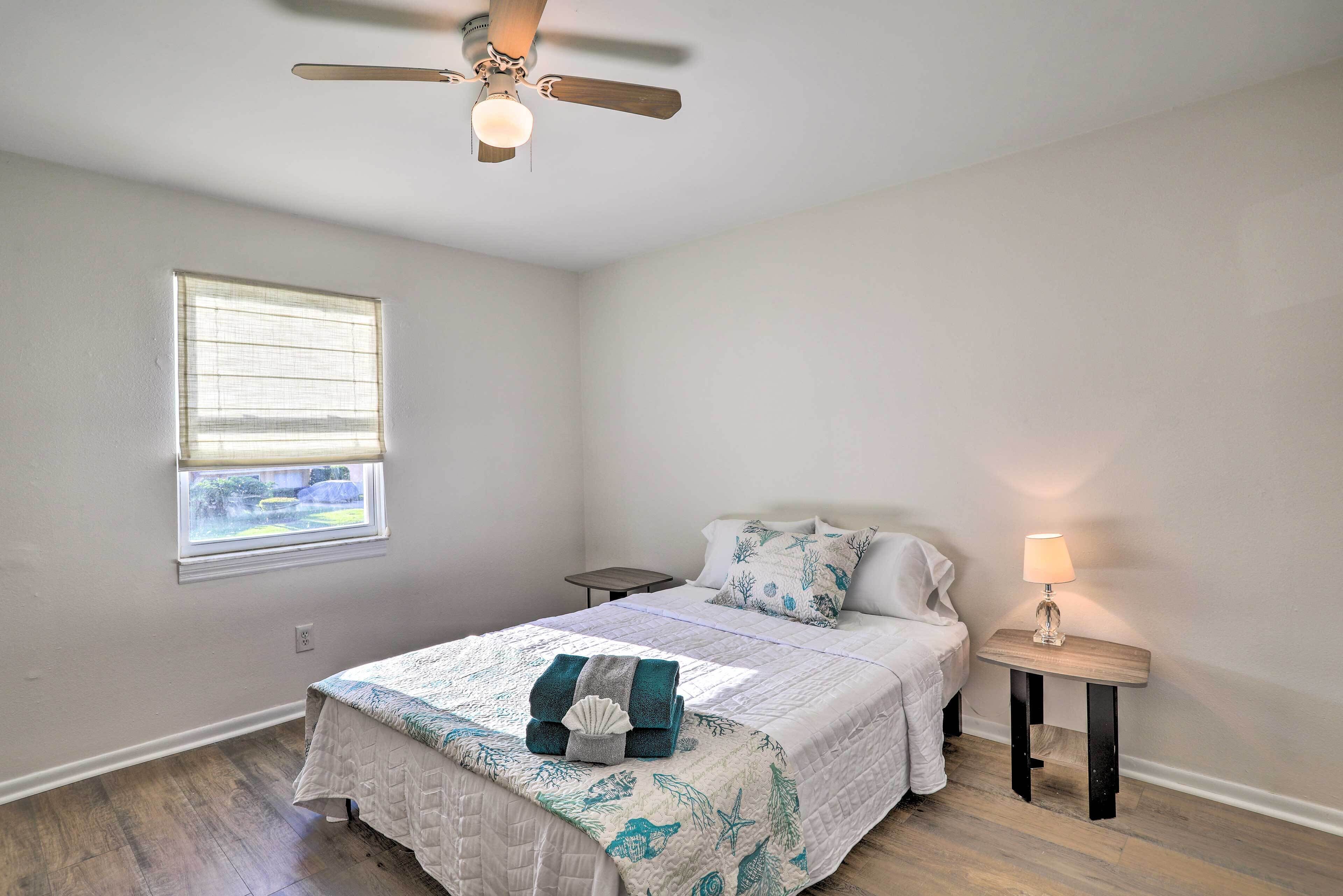 Une chambre à coucher comprenant un lit, une table de chevet, une lampe, un ventilateur de plafond, une fenêtre et une vue sur l’extérieur.