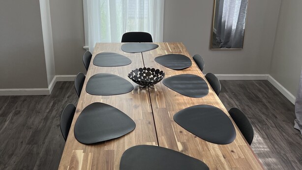 Comedor con mesa de madera, sillas negras, ventilador de techo y ventana con cortinas translúcidas.