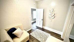 Una sala de estar con un sofá color beige, un tapete estampado y un elemento decorativo con forma de hoja en la pared.