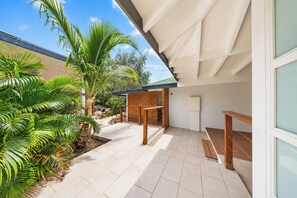A modern outdoor patio with a wooden deck, a stone pathway, and lush tropical plants.