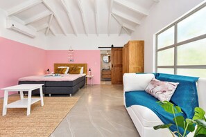 A bedroom with a bed, bedside tables, a sofa, a window, and a bathroom visible through an open door.