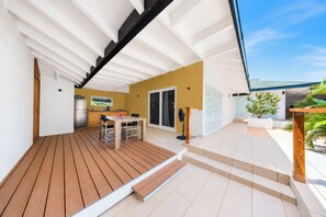 A modern outdoor patio with a wooden deck, a dining table, and a kitchen area.