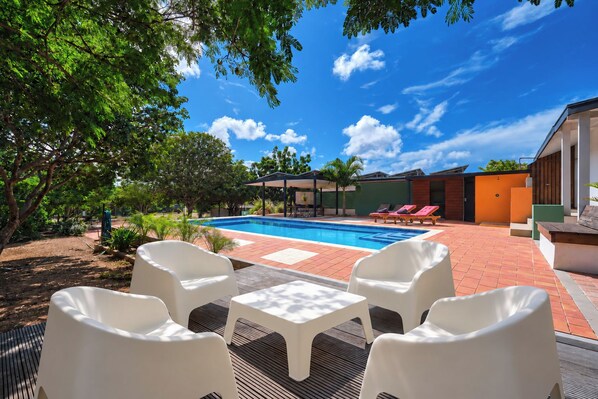 A swimming pool with lounge chairs, a covered seating area, and a patio with outdoor furniture.