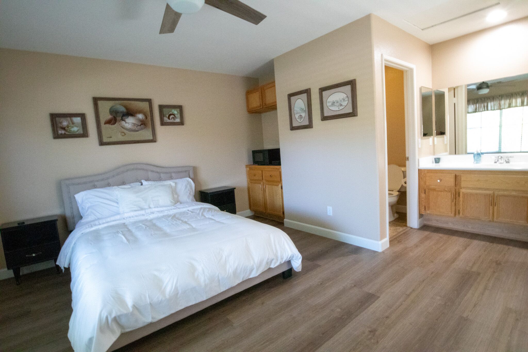 A bedroom with a bed, nightstands, a wooden cabinet, and a bathroom with a vanity and mirror.