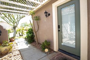 Enter a serene home through the light green door, surrounded by lush greenery and a beautiful trellis.