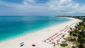 Une plage aux eaux turquoise et limpides, un rivage sablonneux et de nombreux parasols.