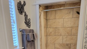 Un baño con ducha, inodoro, lavabo, banca de madera y alfombra estampada.