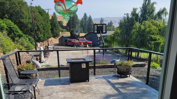 Un patio techado con mobiliario exterior, un aro de baloncesto y vistas a una camioneta roja y árboles al fondo.