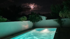 Piscina di notte con una luna visibile e nuvole nel cielo.