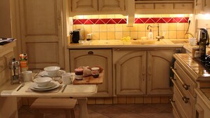 Una cucina compatta con mobili in legno, zoccolo a mosaico e un piccolo angolo ristoro con uno sgabello in legno.