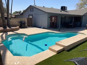 A backyard with a swimming pool, a barbecue grill, and a covered patio area.