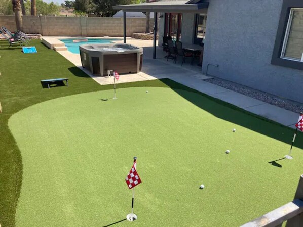 A backyard with a putting green, a hot tub, and a pool.