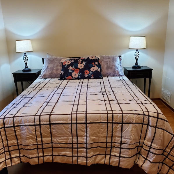A neatly made bed with a plaid bedspread, two bedside tables with lamps, and a floral pillow.