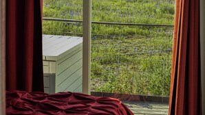 Een slaapkamer met een groot raam dat uitkijkt op een grasveld en bomen.