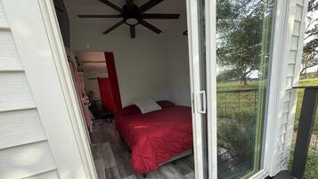 Un dormitorio con colcha roja, ventilador de techo y puerta corrediza de vidrio que da a un balcón.