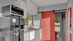 Een moderne keuken met roestvrijstalen apparatuur, witte keukenkastjes en een rode schuifdeur naar een balkon.