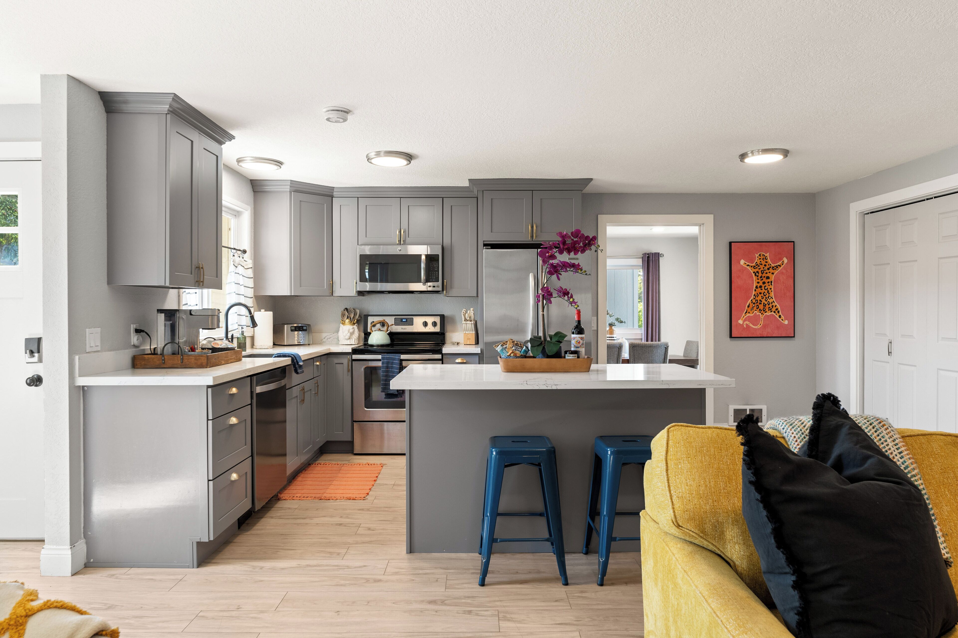 A modern kitchen with grey cabinets, a central island with stools, stainless steel appliances, and a decorative orchid vase.