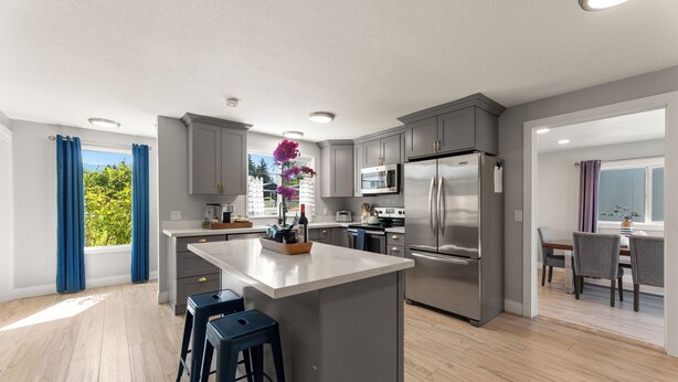 A modern kitchen with grey cabinets, stainless steel appliances, and a central island with bar stools. - Ridge View Retreat with Mtn Views & Hot Tub (Port Angeles)