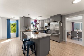A modern kitchen with grey cabinets, stainless steel appliances, and a central island with bar stools. - Ridge View Retreat with Mtn Views & Hot Tub (Port Angeles)