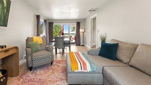 A modern living room with a grey sofa, patterned armchair, and a colorful striped throw. A dining area is visible in the background with a table and chairs. - Ridge View Retreat with Mtn Views & Hot Tub (Port Angeles)