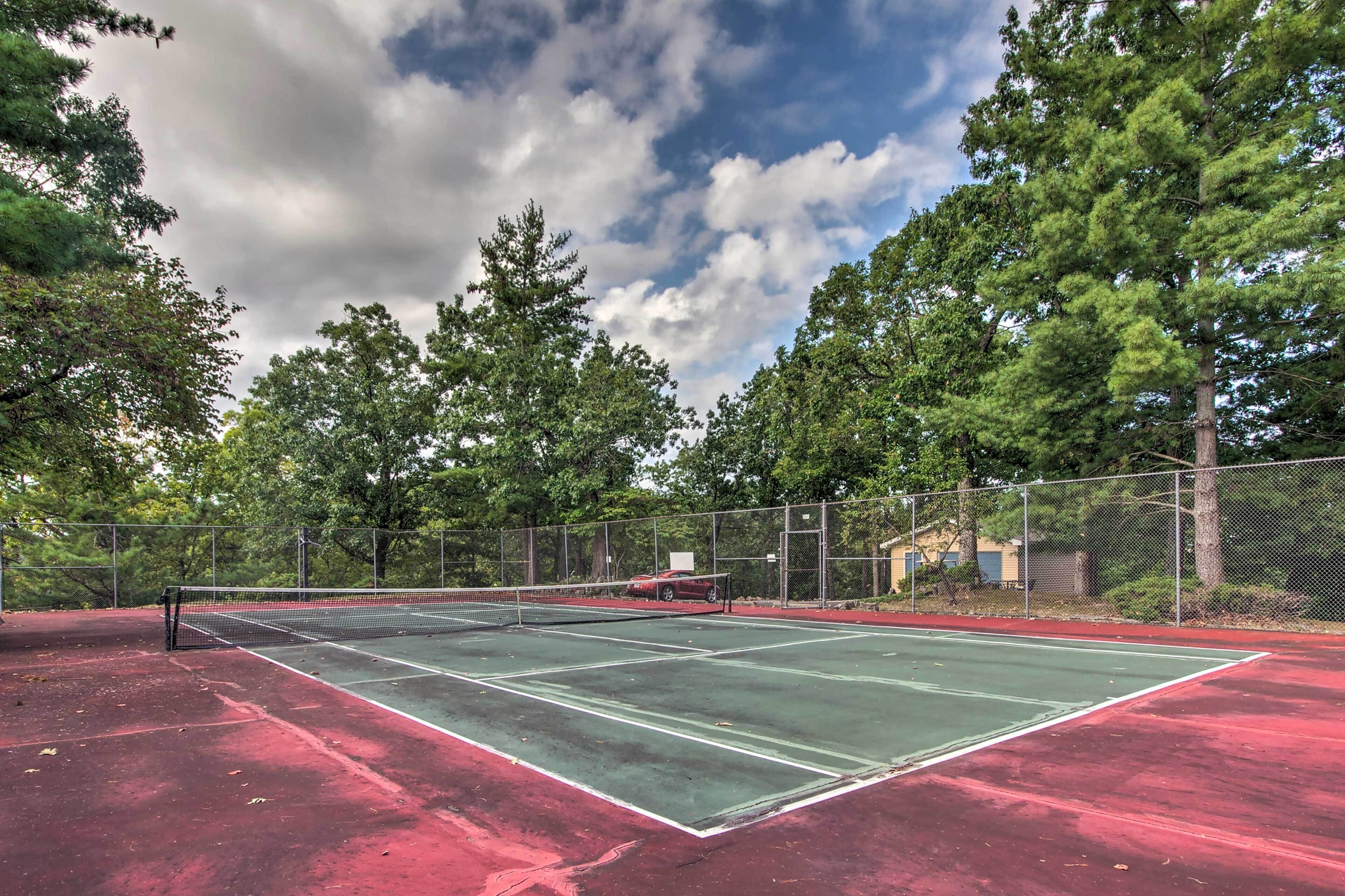 Un court de tennis en plein air, entouré d’arbres et délimité par une clôture.