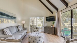 Ein Wohnzimmer mit einer Couch, einem Hocker, einem Sessel und einem flachbildfernseher an der Wand.