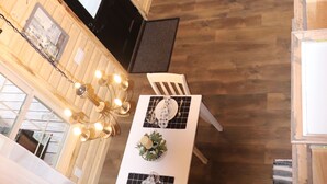 Un interior de madera con comedor, una araña y un ventanal con cortinas.