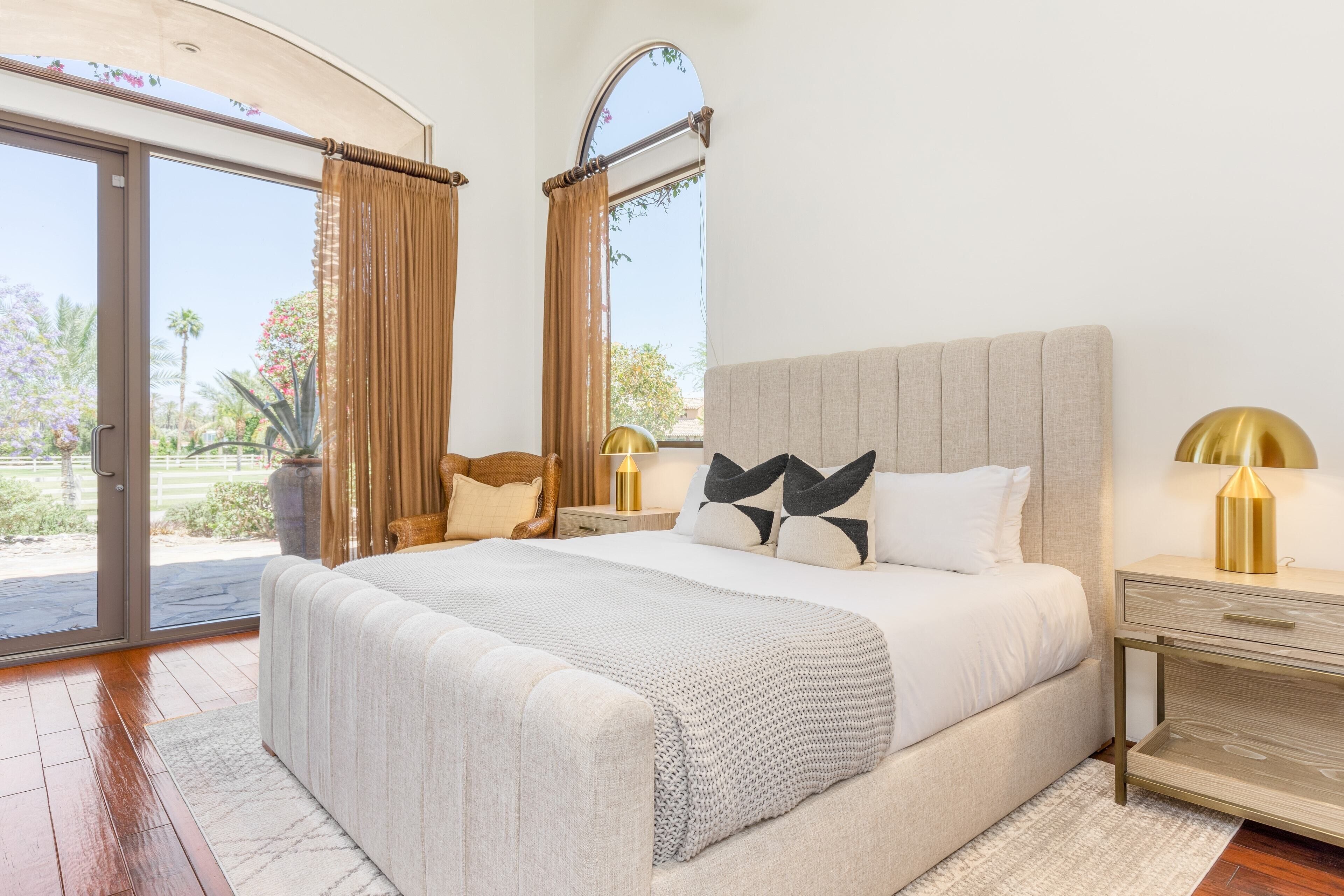 A bedroom with a large bed, a nightstand, a lamp, and a view of the outdoors.