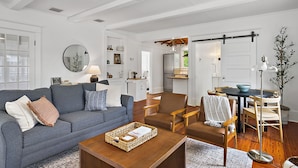 A spacious living room with a grey sofa, a brown leather chair, a wooden coffee table, and a dining area with a table and chairs.